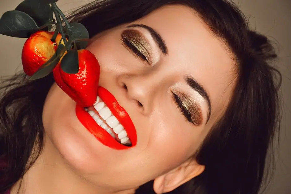 Close-up of a woman with vibrant makeup and red lips smiling next to artificial strawberries.
