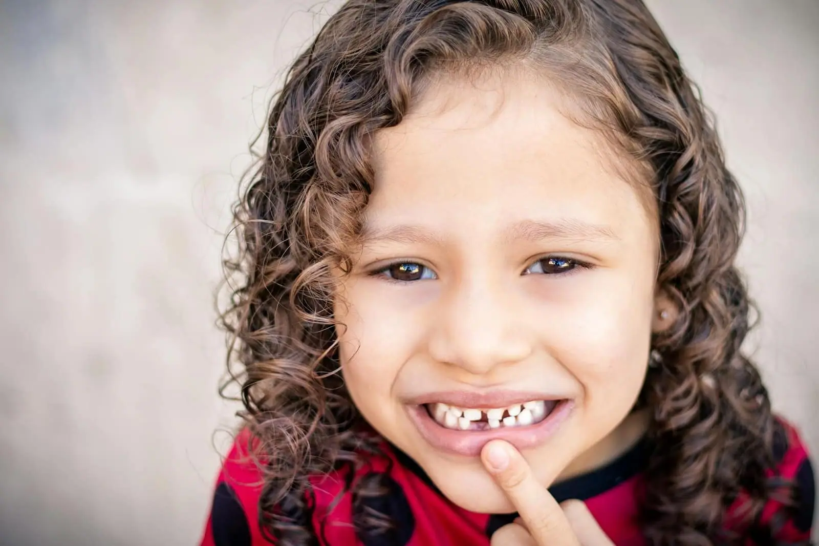 Close-up of a smiling child with curly hair showing a missing tooth, conveying happiness.