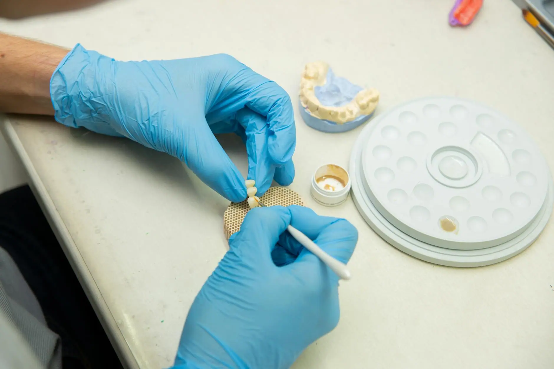 From above of crop anonymous orthodontist in latex gloves making fake teeth for denture in modern dental clinic