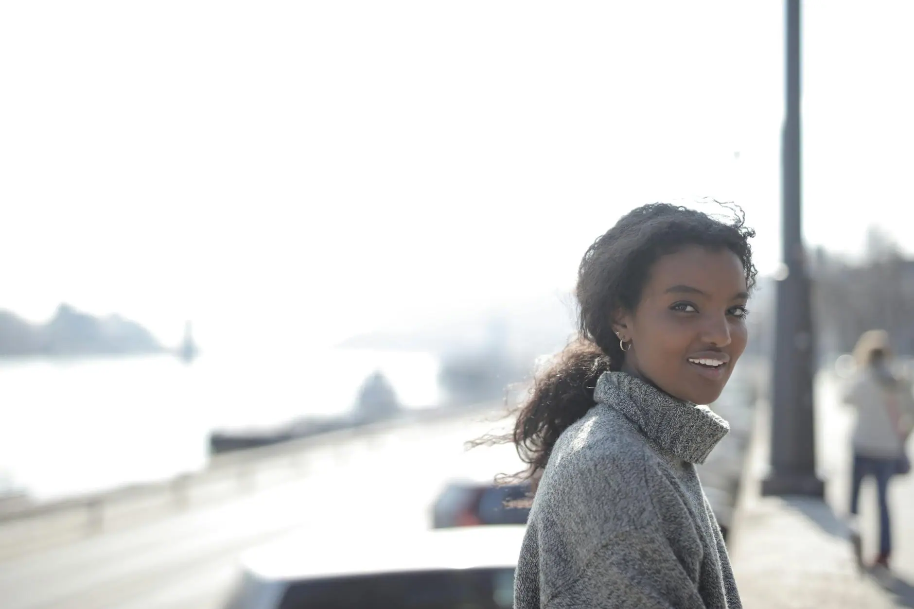 Portrait of a smiling woman outdoors in a cozy grey sweater on a bright day.